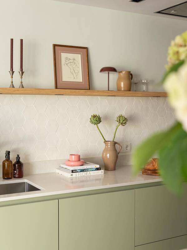 Keuken met witte zeshoekige Hexa White-wandtegels, lichtgroene kastjes, een houten plank en roze accessoires.
