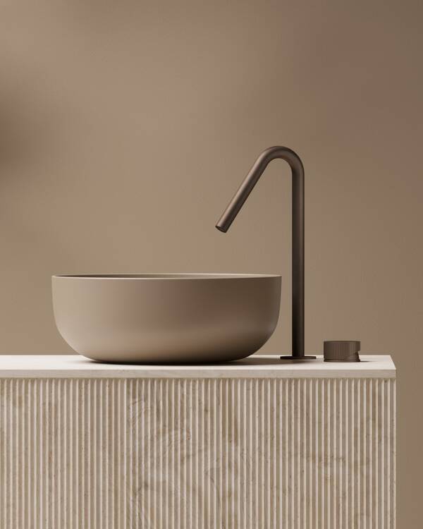 Hotbath Guy wastafelkraan in Tuscan Bronze naast een beige waskom op een licht meubel met verticale groeven.