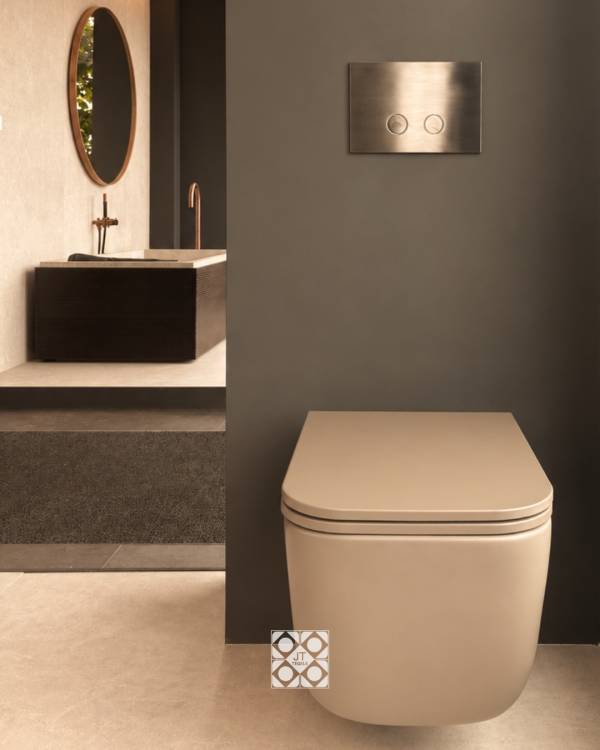 Zandkleurige toiletpot tegen een donkere wand, met daarnaast een maatwerkbad en ronde spiegel in warme tinten.