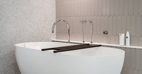 Terrazzolooktegels naast beige accenttegels achter een wit bad bij TONSCHOLTEN. Tegels & Sanitair in Uitgeest