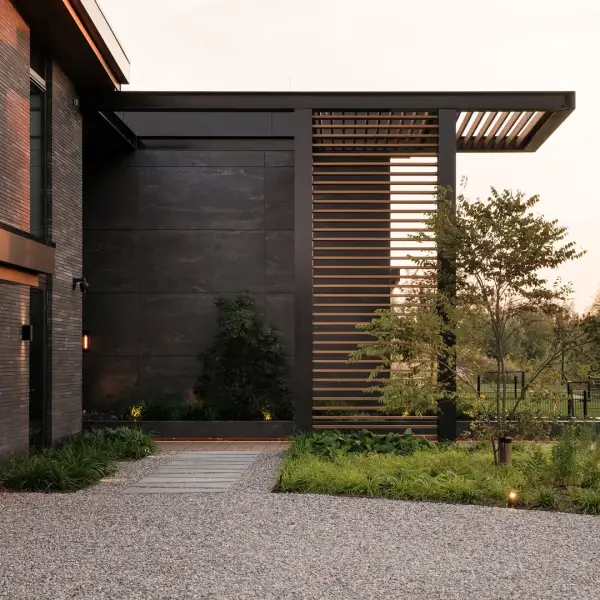 Donkere keramische gevel van een moderne villa met horizontale lamellen, een overkapping en groene tuin.