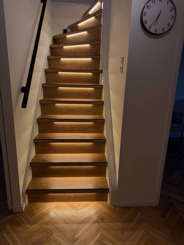 PVC-trap met bruine houtlook, verlichte trederanden en zwarte leuning bij Prime Interieur in Den Haag