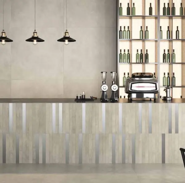 Barinterieur met grijze betonlooktegels, een front met verticale stroken, zwarte hanglampen en verlichte flessenrekken.