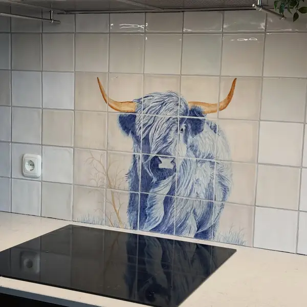 Handbeschilderd tegeltableau met een Schotse hooglander in blauwtinten op witte tegels achter de kookplaat.